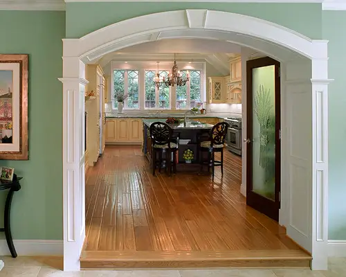 Dining room with wooden floors viewed through an archway.
