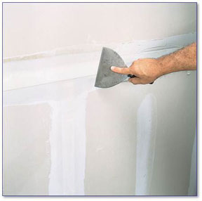 Hand showing joint knife smoothing drywall.