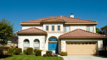 Photo of the front of a large two story house with an attached garage and a green, manicured lawn.