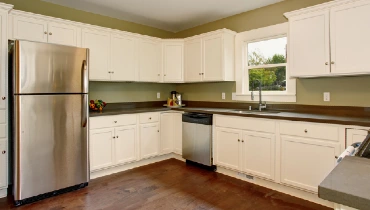 Photo of a large kitchen with white cabinets and a dark wooden floor.