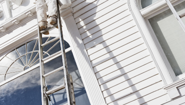 Exterior of a home being painted by a painter on a ladder.