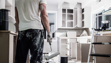 Man standing in kitchen holding a dirty paint roller.