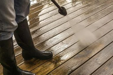 Person in boots power washing wooden deck.