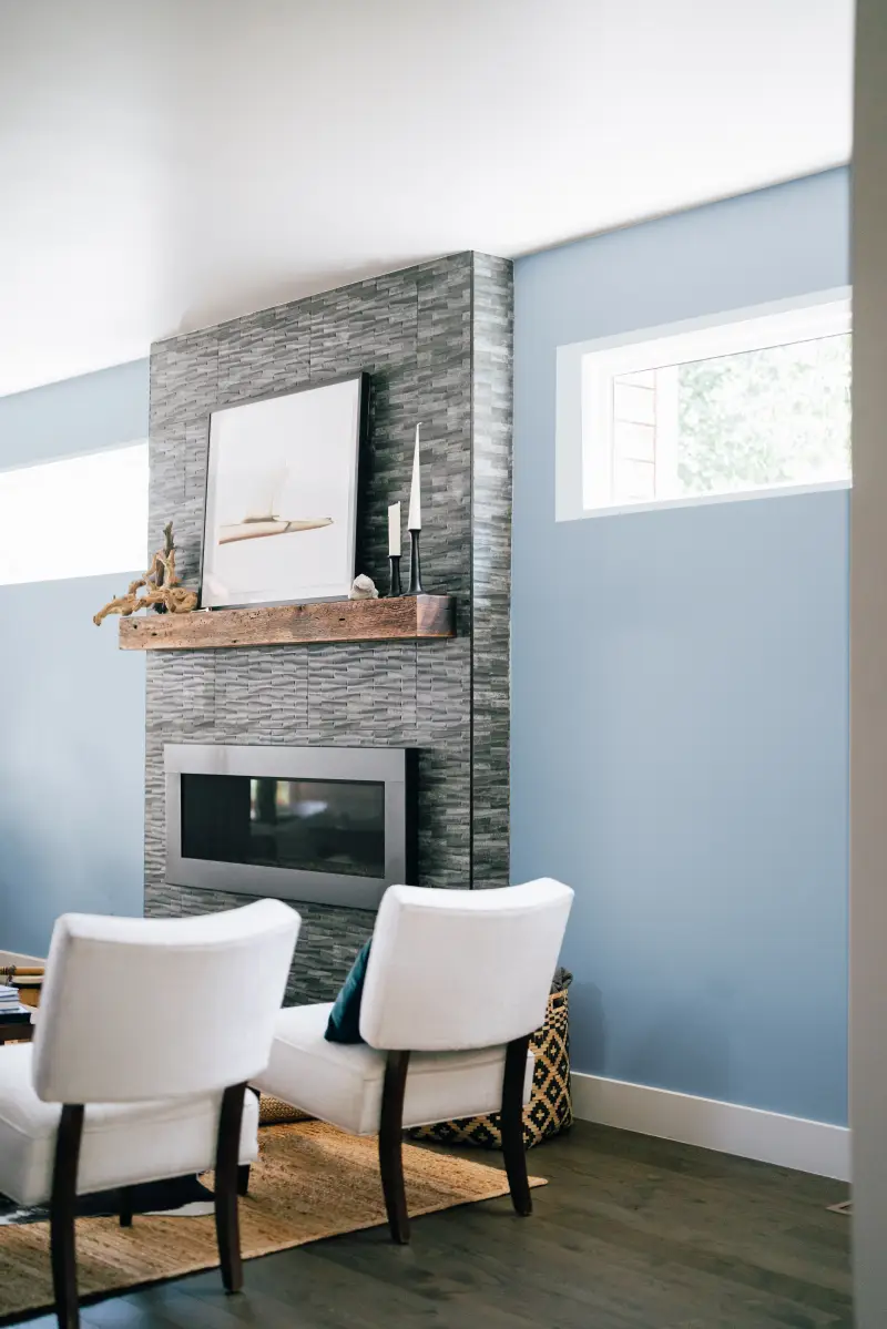 Cropped view of electric center fireplace with painted gray brick, sky blue walls, and boho decor.