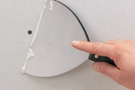 Hand holding a joint knife next to a screw.